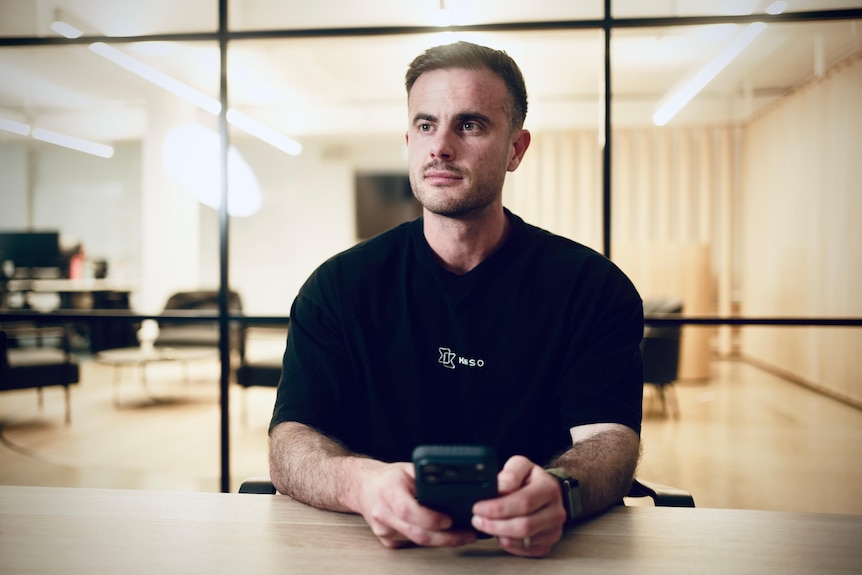 Man in black t-shirt looks past the camera sitting in office.