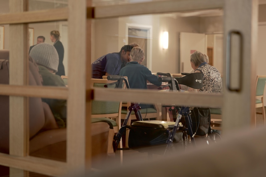 A group of residents sit around a table in the dining hall at an aged care facility.