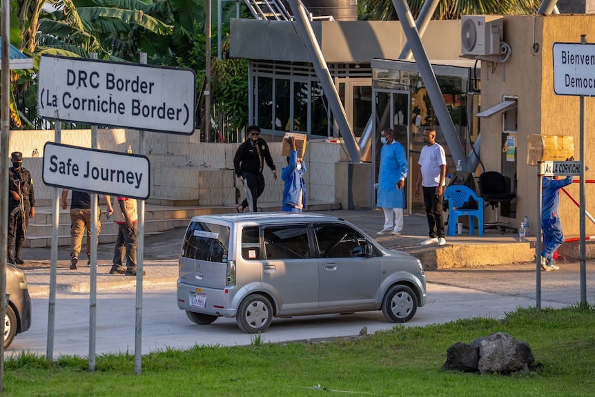 A health worker standing at the DRC-Rwanda border as cars queue to cross.
