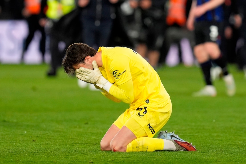 Soccer goal keeper falls to his knees, head in his hands, upset at full-time