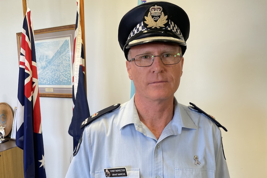 A man in a police uniform standing in front of some flags in a foyer.
