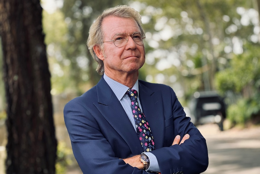 Shane Oliver stands with arms folded, with trees behind him.