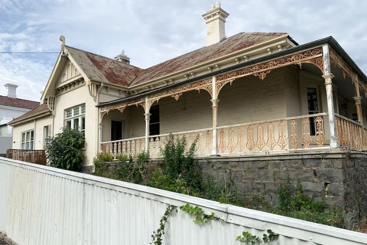 a gloomy cream-coloured house with a rusted roof and iron balcony