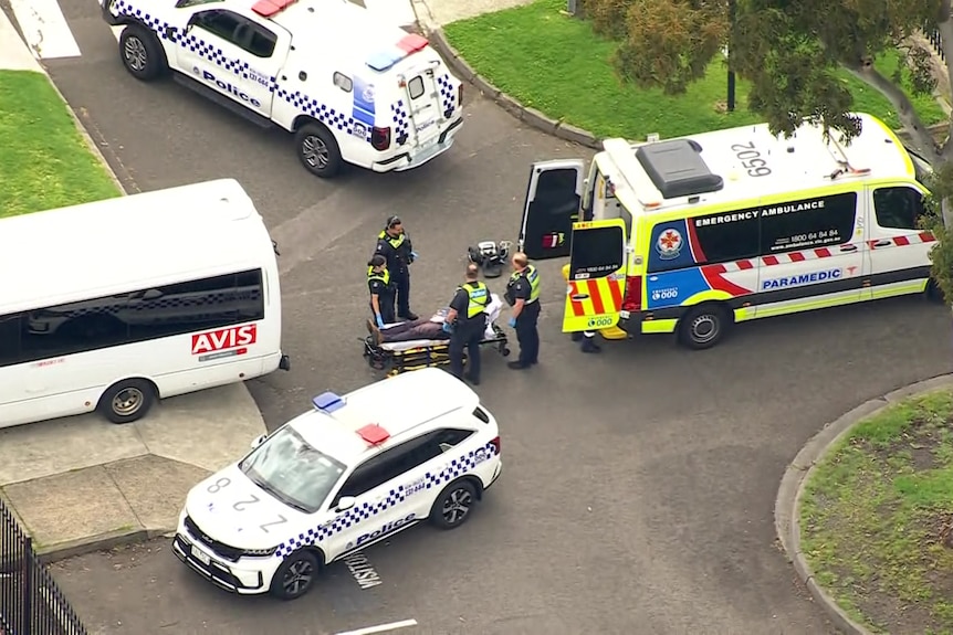 An aerial shot of a person on a stretcher near an ambulance and police cars surrounded by police officers.