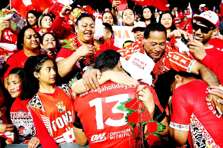 Jason is embraced by fans after a rugby league match in a sea of red jersies.