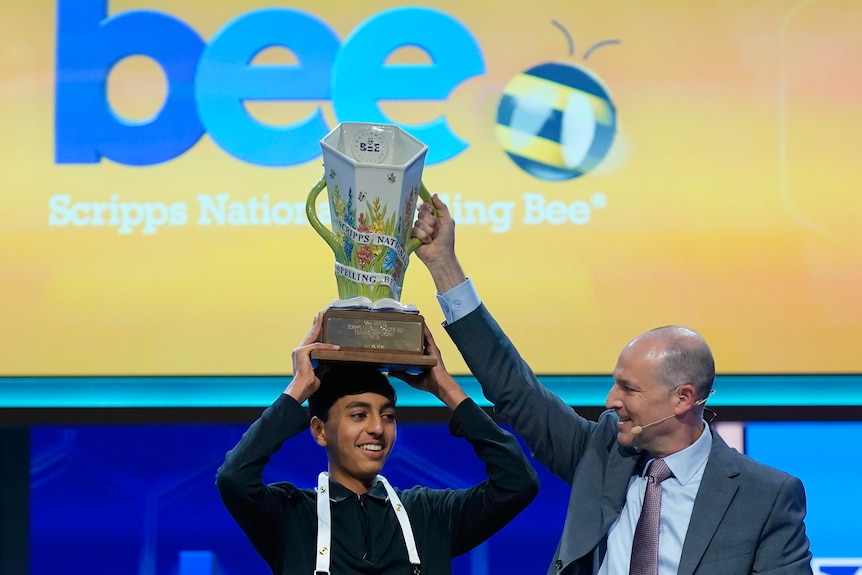 A teenage boy holds a trophy on his head, next to an event official