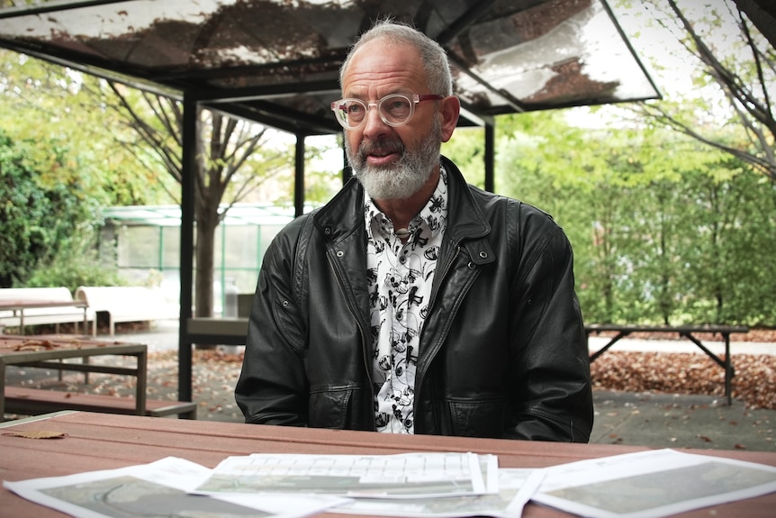 Man in glasses and leather jacket sits in leafy environment