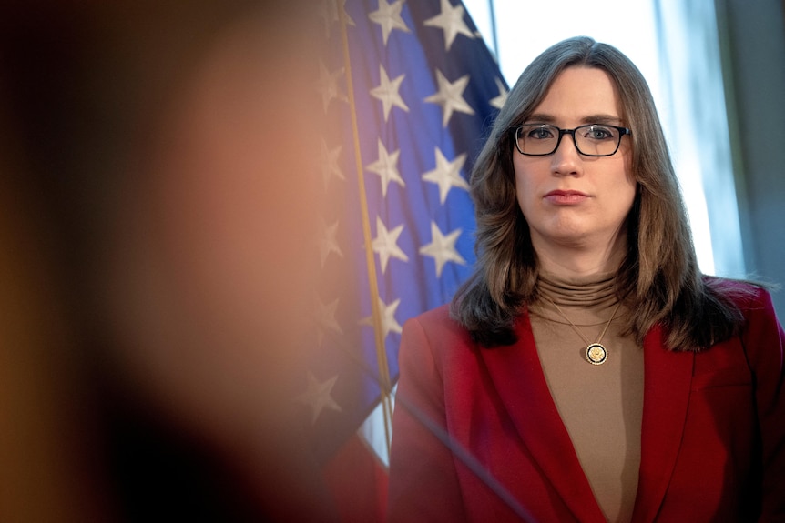 Woman in red blazer stands in front of American flag