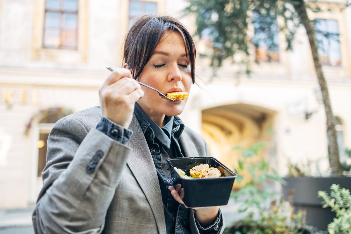 Woman closing eyes enjoying meal from a takeout box outdoors
