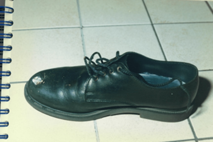 A close-up police photograph of a leather shoe with damage from a bullet.