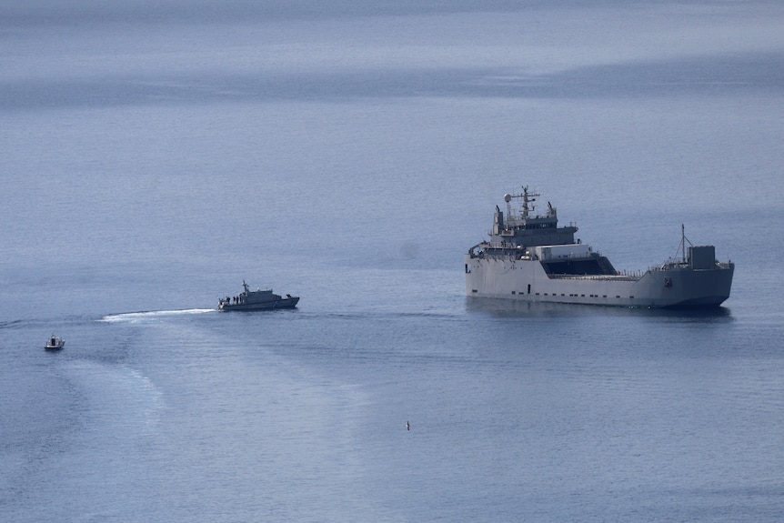 A small boat approaches a large vessel in the ocean.