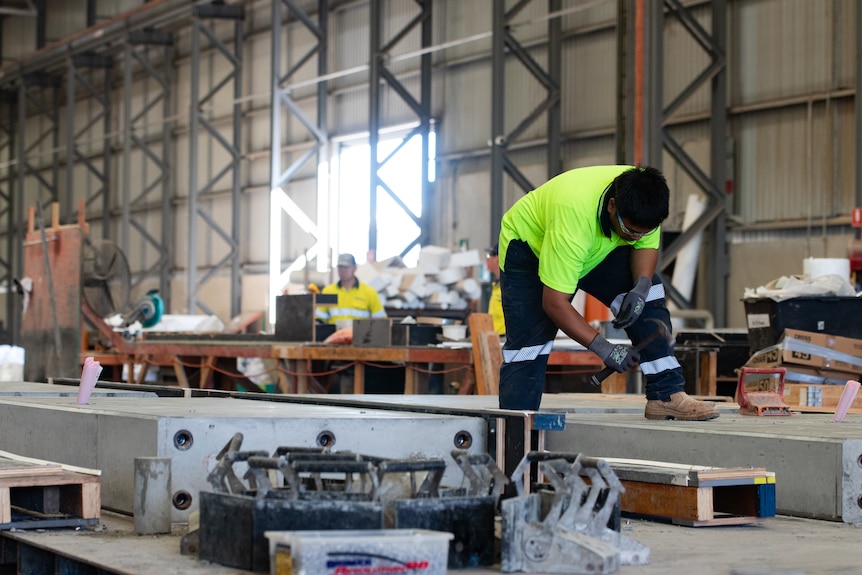 A man works on a pre-fab home in a giant shed