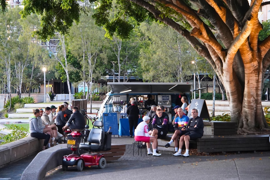 A person runs along the Brisbane River in South Bank with people sitting at a coffee van in the background.
