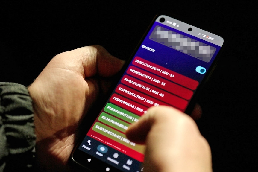 A close up of hands holding a phone in the dark. Its screen shows a list of numbers with different colour sections.