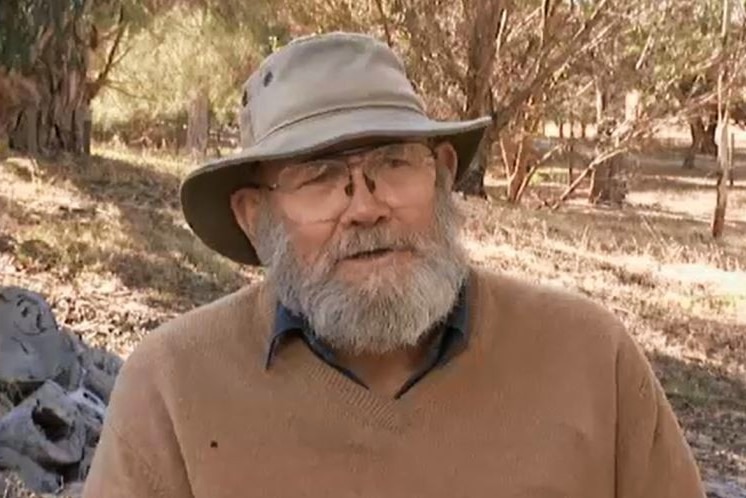 A man with big glasses, bear and soft hat in a bushland setting