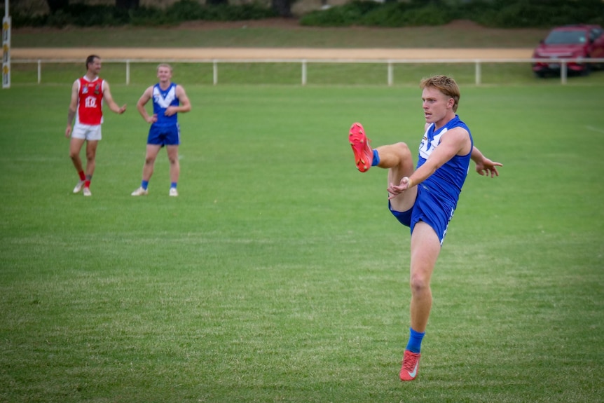 A footballer in a blue jumper and shorts kicks for goal
