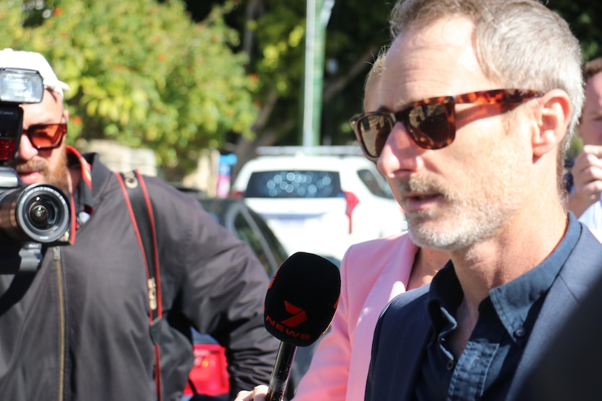 A close up of Craig Silvey who wears sunglasses as he wades through a media pack
