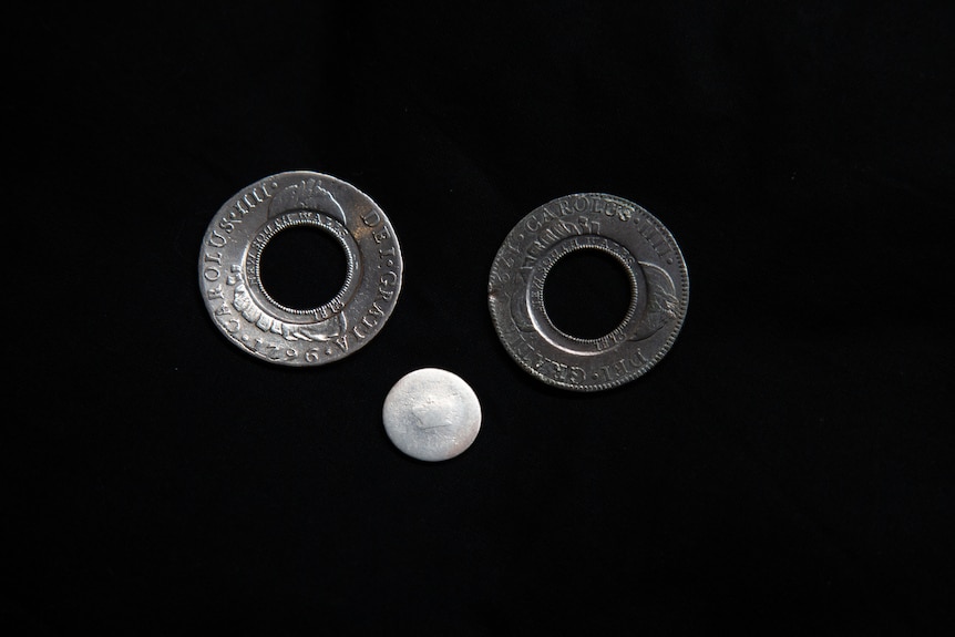 A close up photo of three silver coins, two with their middles punched out