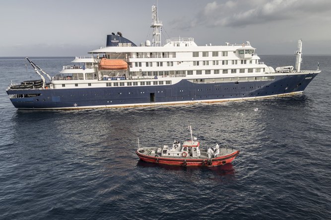 An aerial view of an ambulance boat carrying crew members wearing hazmat suits as they approach the pilot door on the starboard side of the cruise ship MV Hondius, while stationary off the port of Praia, the capital of Cape Verde, on May 5, 2026. Two seriously ill crew members on a cruise ship stricken by a deadly hantavirus outbreak will be evacuated via Cape Verde to the Netherlands, allowing the vessel to sail on to Spain's Canary Islands, the ship operator said Tuesday.
The MV Hondius has been at the centre of an international health scare since Saturday, when WHO was informed that the rare disease -- usually spread from infected rodents typically through urine, droppings and saliva -- was suspected of being behind the deaths of three of its passengers.
As others fell ill, passengers and crew have been in isolation after Cape Verde authorities barred the ship from docking, and as health authorities scrambled to find a port that would take the Hondius. (Photo by AFP)