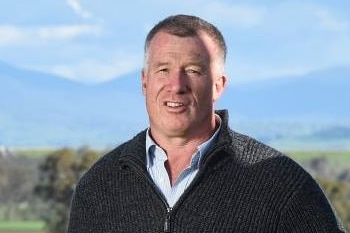 A man standing with his hands in his pockets in front of a farm.