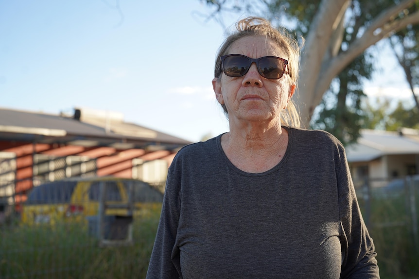 An older woman in sunglasses looks at the camera outside.