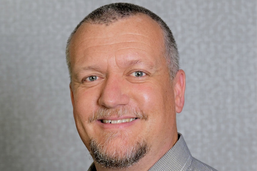 A man with short grey hair and blue eyes smiles at the camera.