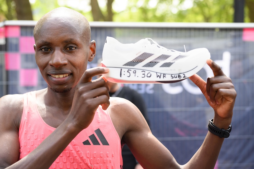 Runner Sabastian Sawe holds up a white Adidas running shoe.