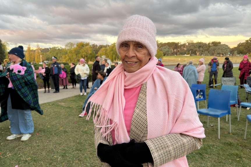 Ngunnawal Elder Aunty Violet Sheridan in warm, pink clothes, looks at the camera, standing near a vigil.