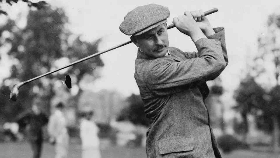 A black and white picture of Harry Vardon with a golf club. He's wearing a flat cap and tweed jacket.