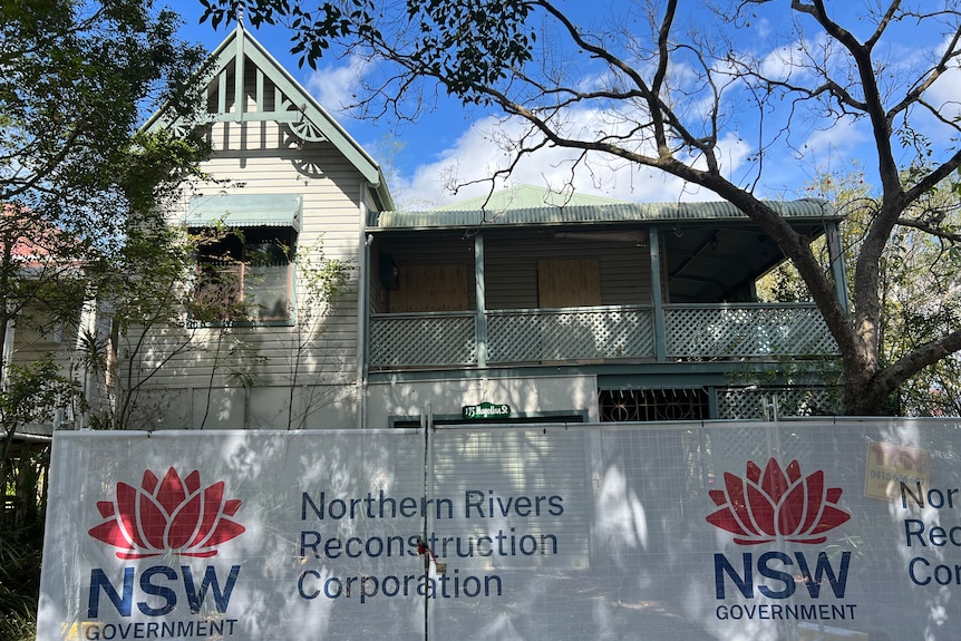 weatherboard two storey home with mesh security fence around it with Northern Rivers Reconstruction Corporation signage
