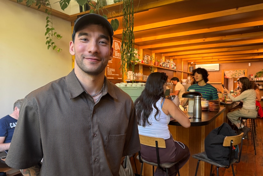 Man in shirt and cap standing in front of the cafe bar.