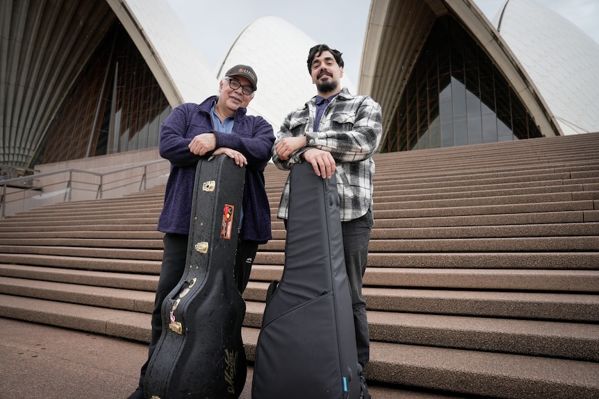 Buddy and Goori standing at the steps of the Sydney Opera House with guitars.