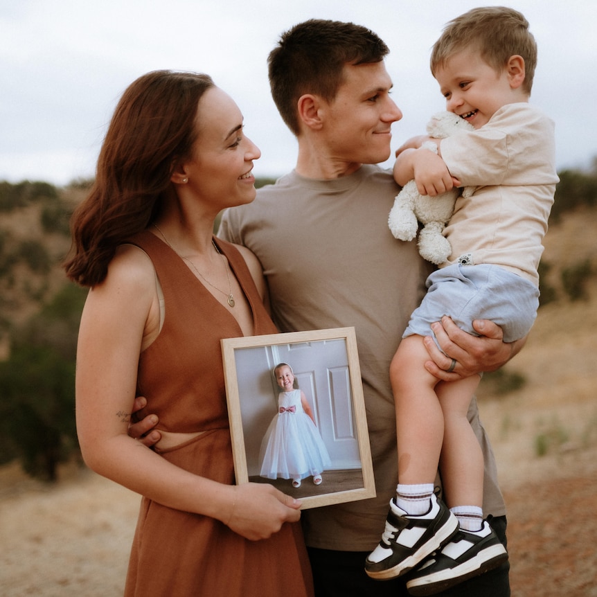 A mum, dad, son and photo of daughter altogether outside in nature