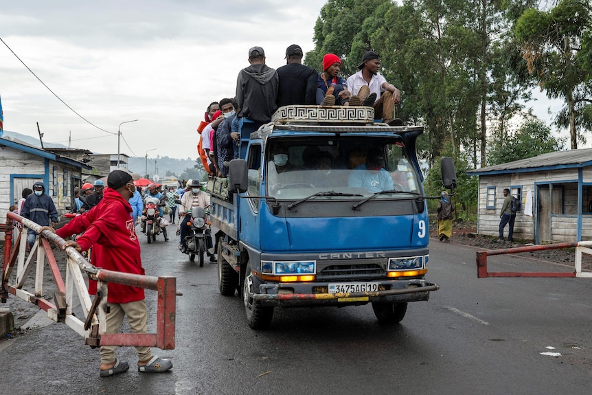 A group of young men packed onto the back of a blue pick-up truck pass through a road barrier.