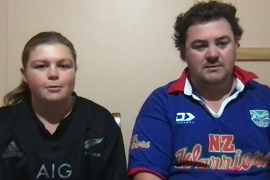 One woman wearing black shirt and man wearing blue shirt both sitting down looking at camera