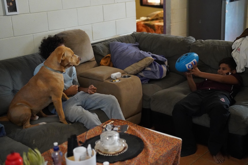 Two boys sit on a couch with a dog and a football.