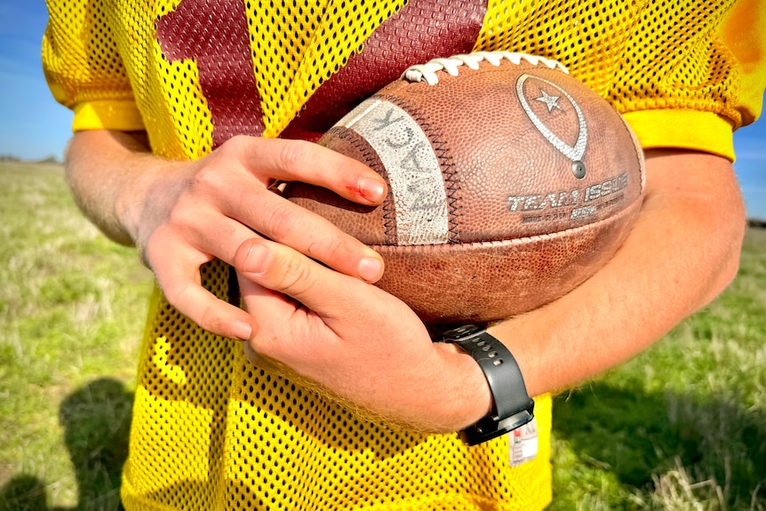A red headed 19-year-old boy with a football on a farm.