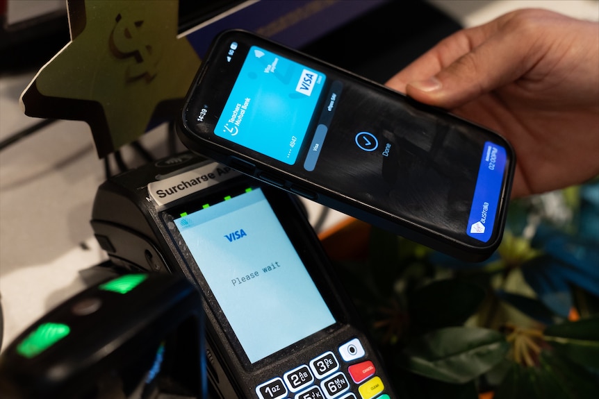 A hand waves a phone showing a credit card app over an eftpos machine.