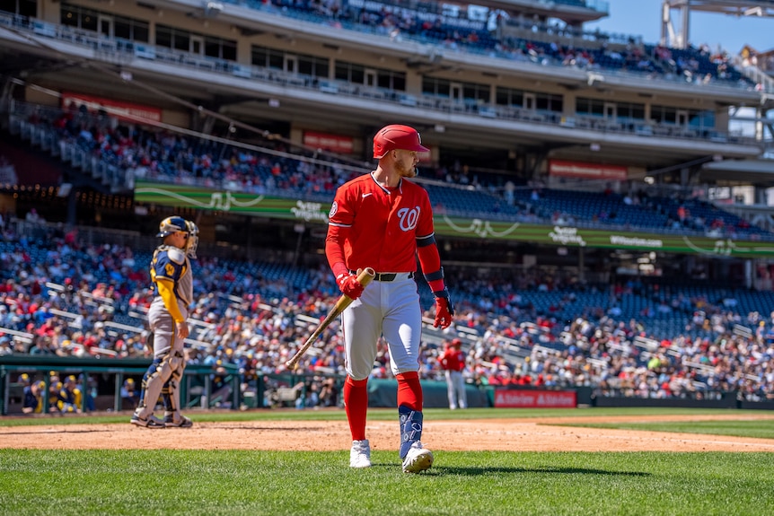 Curtis Mead, wearing red kit, walks off the field with his bat during a baseball game.