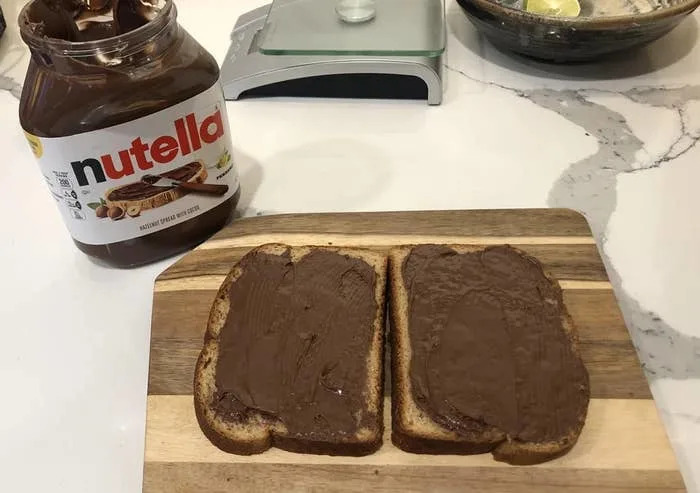 Nutella jar and two slices of bread spread with Nutella on a cutting board