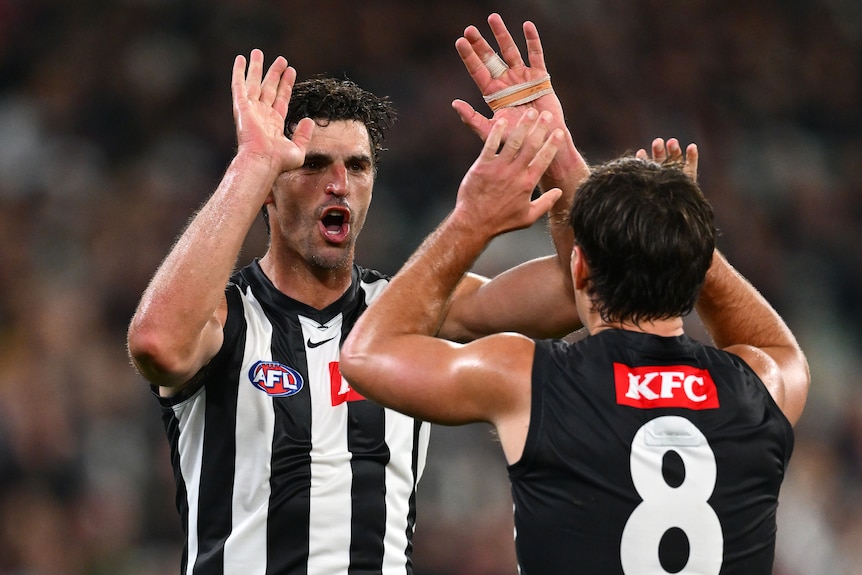 Two AFL players in white and black high five with hands above their heads