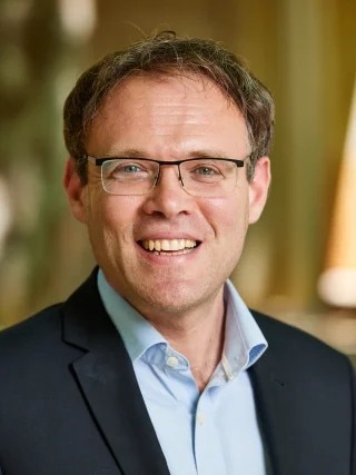 A professional headshot of a man smiling.