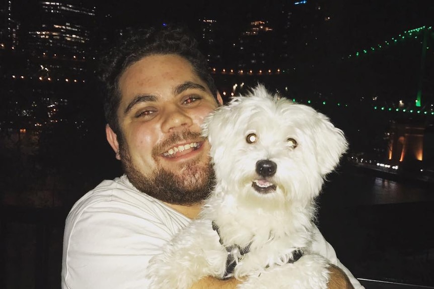 A man in white t-shirt holding a white dog and smiling at the camera