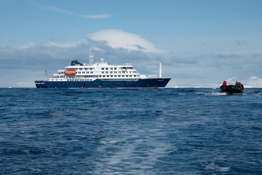 A cruise ship on the open ocean with a smaller dinghy approaching.