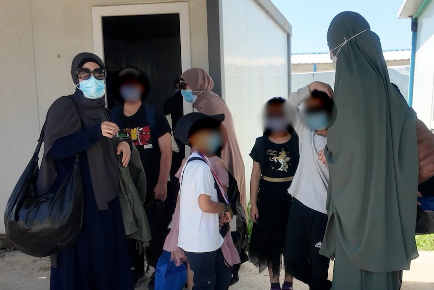 A group of women wearing hijabs and face masks, accompanied by a group of children.