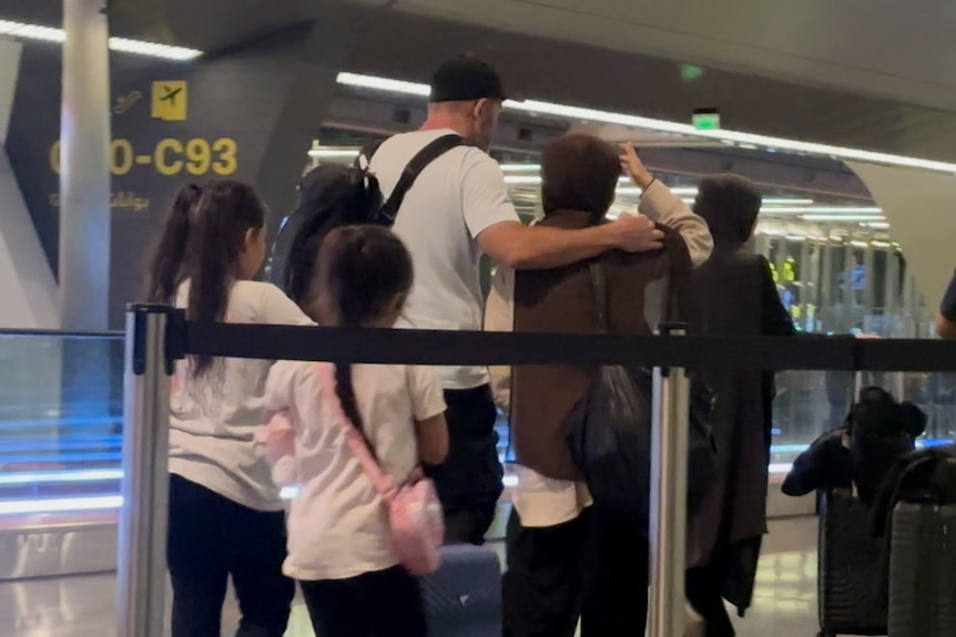 A group of women and children and a man walking through an airport terminal.