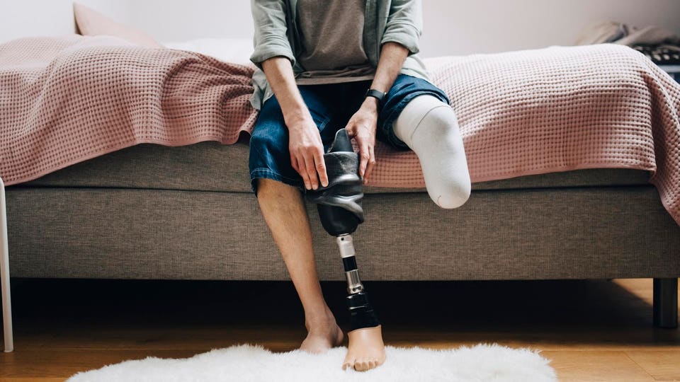 Low section of disabled man with prosthetic leg sitting on bed at home