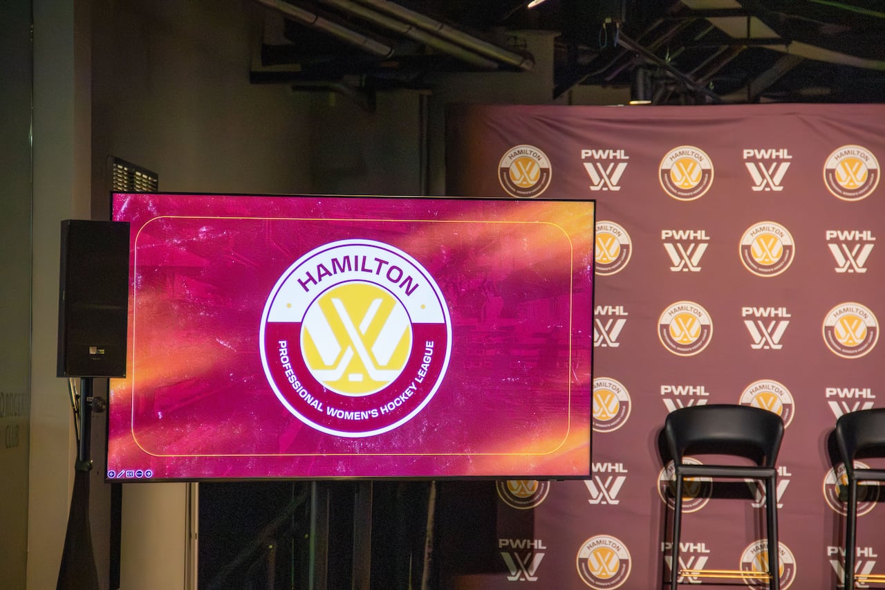 A stage with a screen in front showing a PWHL Hamilton logo in front of a PWHL Hamilton backdrop.