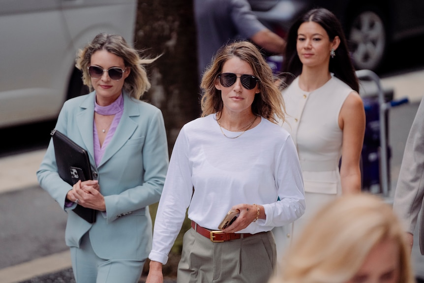 Sall Grover wears sunglasses and wears smart clothes while walking with two other women.