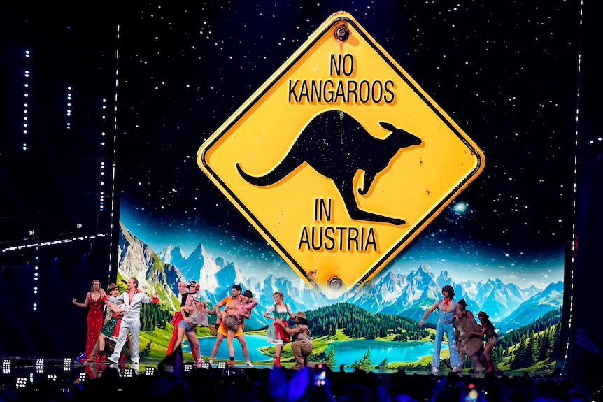 a giant 'no kangaroos in austria' sign is projected behind dancers on a stage